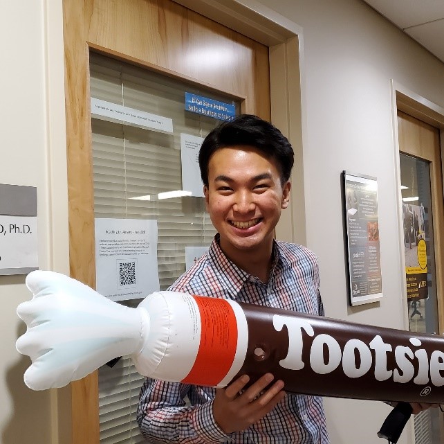 An international student smiling and celebrating the turning in of his I.S., holding a large, inflatable Tootsie Roll.