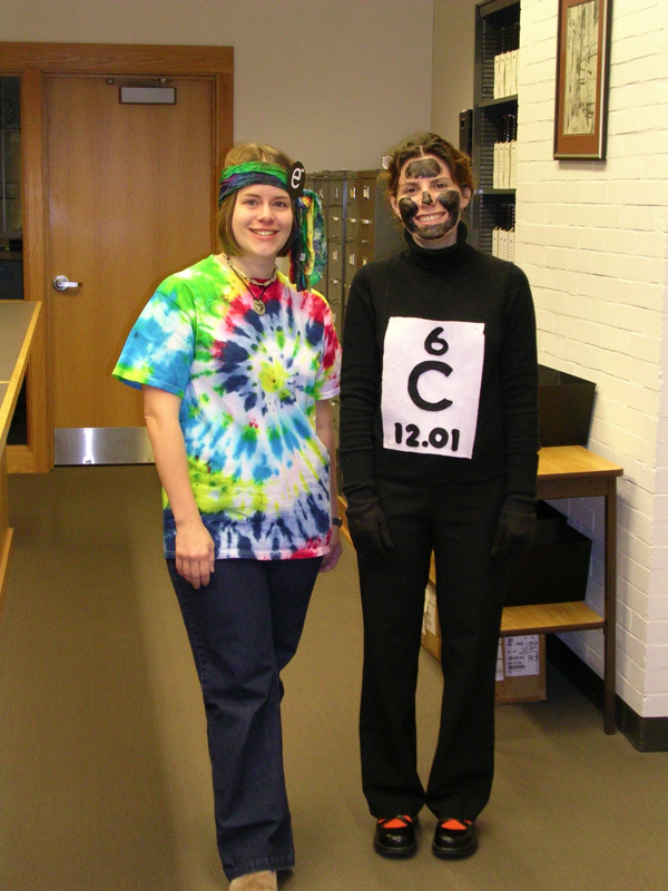 Sarah Sobeck with Melissa Schultz in Halloween Costumes.  Dr. Sobeck is wearing a tie dyed shirt and head band and Dr. Schultz is wearing all black with the periodic information for carbon.