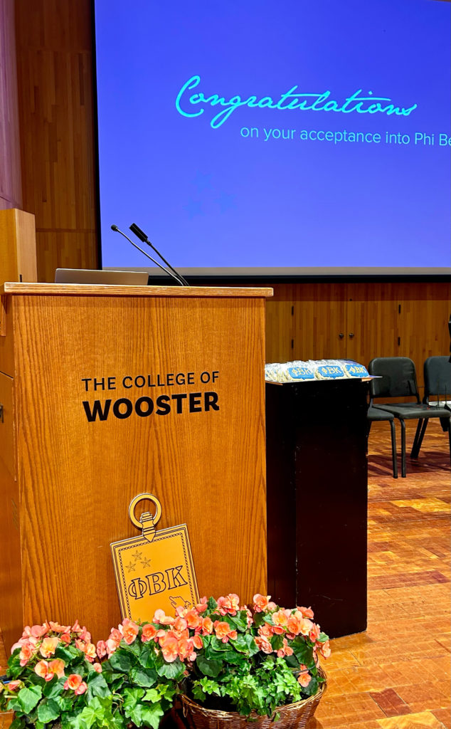 podium in Gault Recital Hall with the College of Wooster and a PBK key with a projector screen reading Congratulations