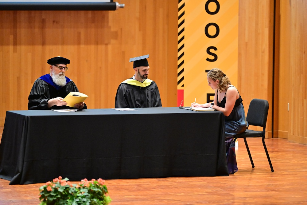 a PBK inductee signs the book on stage as two men look on