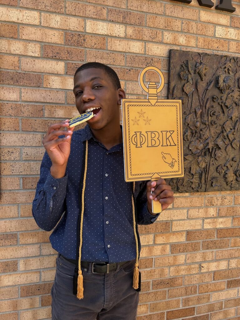 a 2025 Inductee holding the PBK key bites a cookie and smiles at the camera in Scheide Music Center