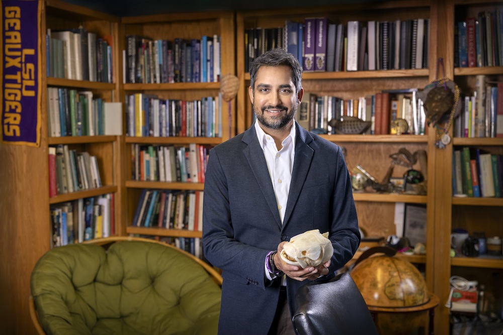photo of Dr. Prosanta Chakrabarty holding a fish skull standing in an office lined with bookshelves